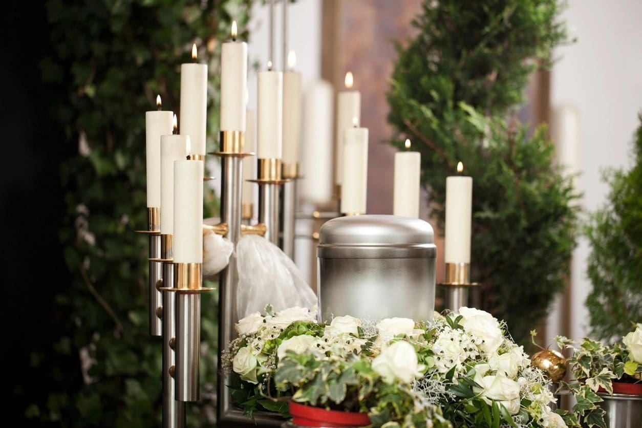 A bunch of candles are lit in front of a urn.