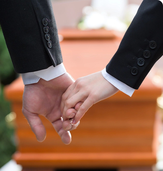 Two people holding hands in front of a casket.