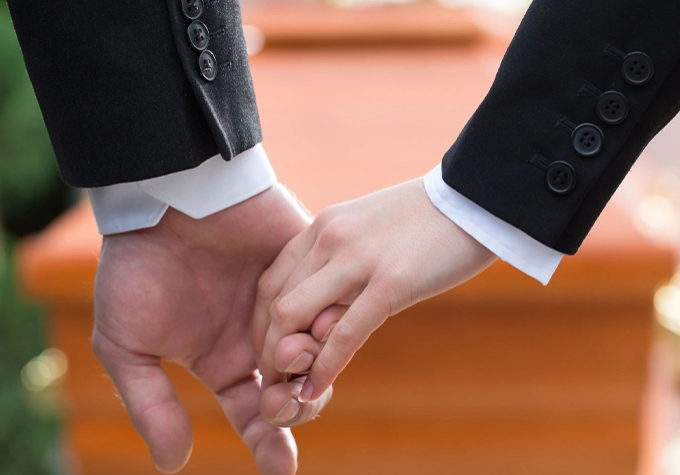 Two people holding hands in front of a casket.