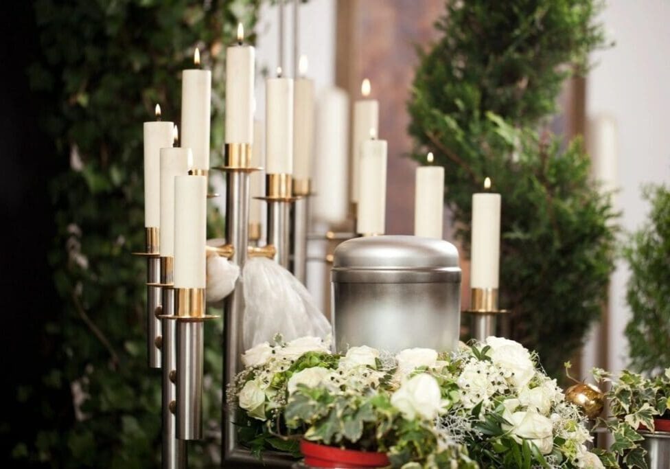 A bunch of candles are lit in front of a urn.